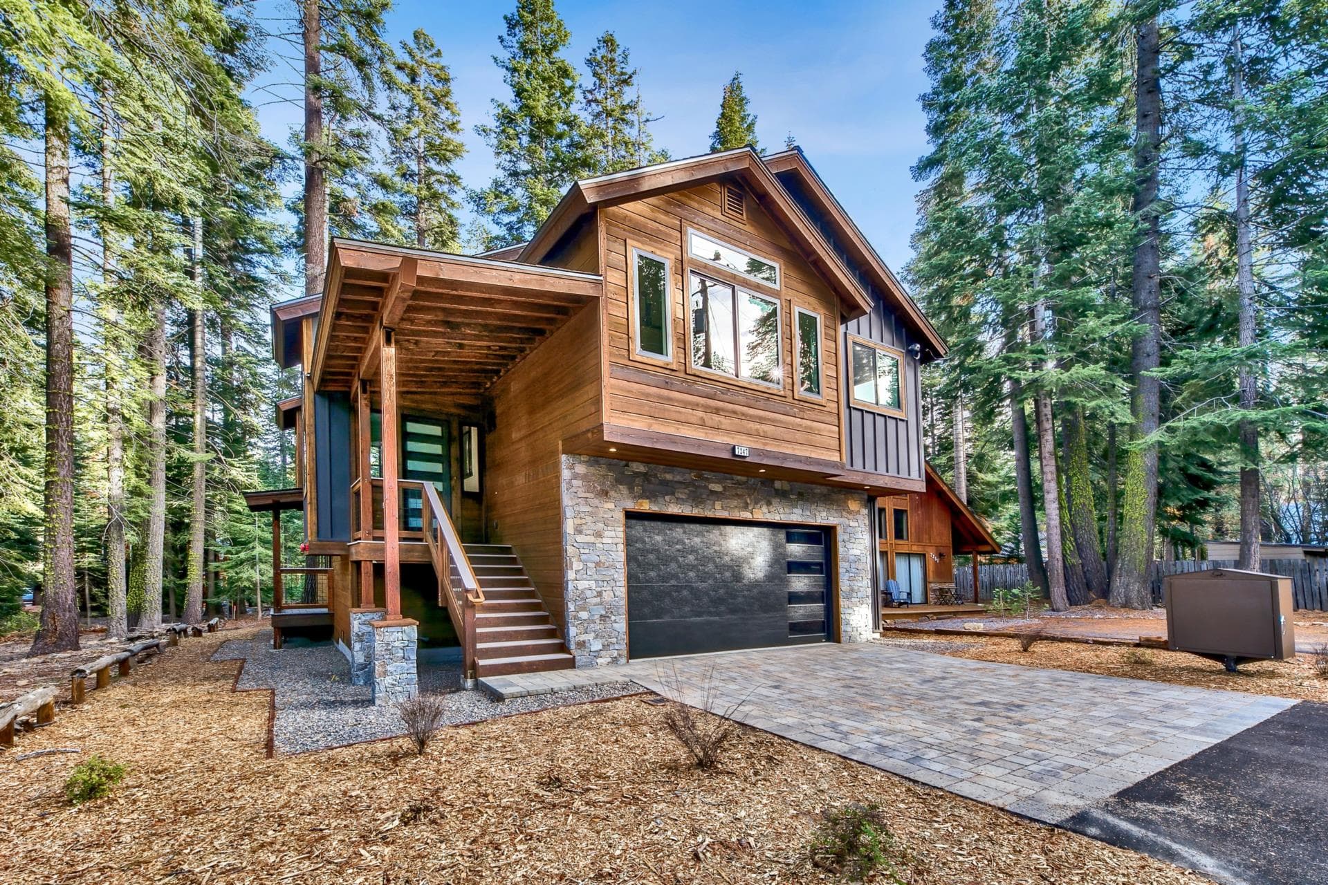 Modern cedar and stone custom home set among tall pines on a sunny day.